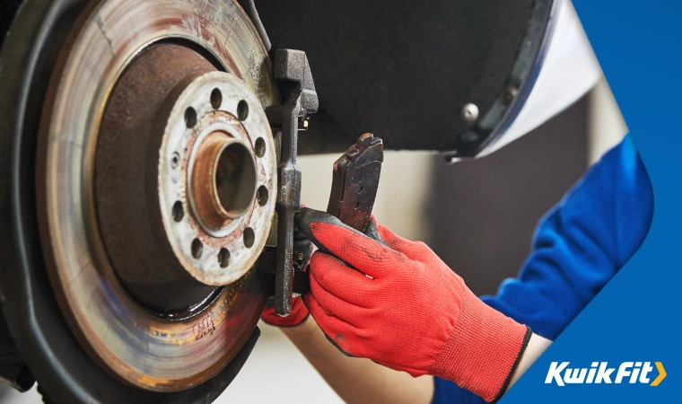 Mechanic wearing red gloves removing a worn car brake disc.