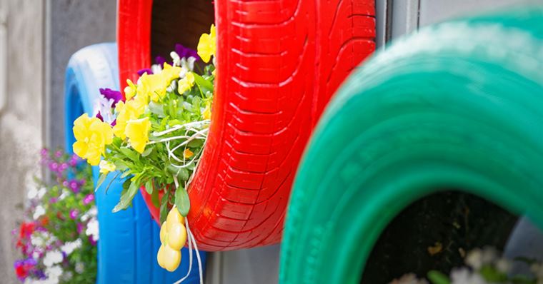 red, green and blue tyres hanging on a wall with plants inside them