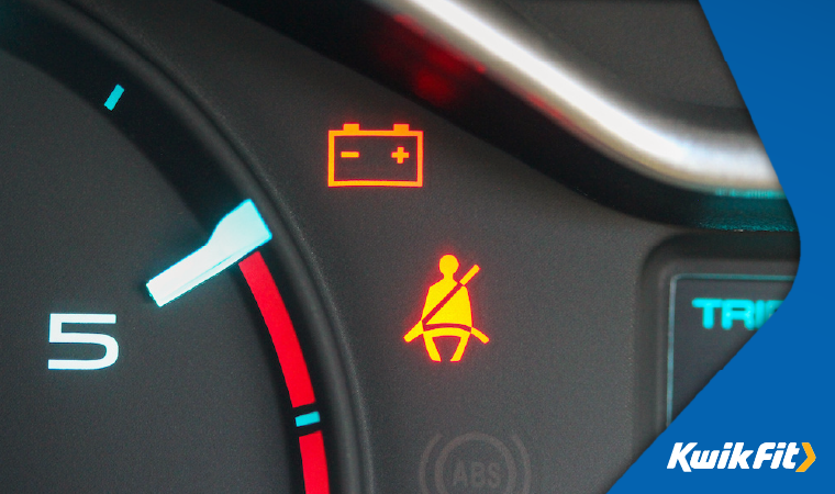 Amber battery voltage warning light and seat belt warning light showing on a vehicle dashboard.