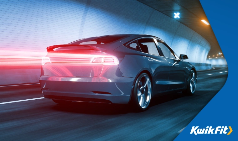 A sleek, modern all-electric car drives through an underpass  its tail-lights creating a streak behind it.
