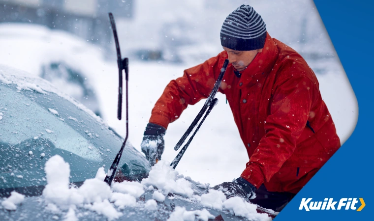 Man in red winter jacket is scraping ice of his car.