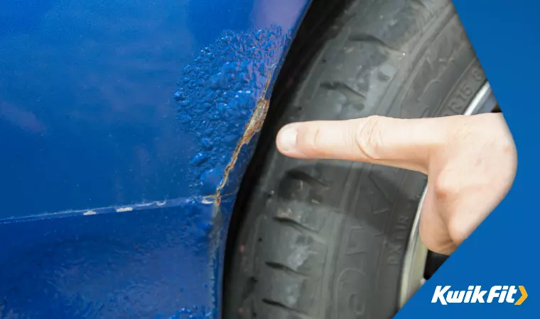 A finger points to rust bubbling through paintwork on a car's wheel well.