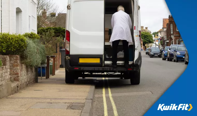 A white commercial van is illegally parked on the pavement in a double yellow line section while offloading.