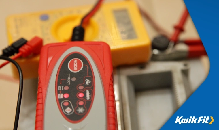 Close up of red smart battery charger connected to a car battery as part of routine maintenance.