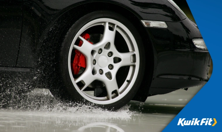 Sports car with well-maintained red brake caliper engaging ABS in rainy weather.