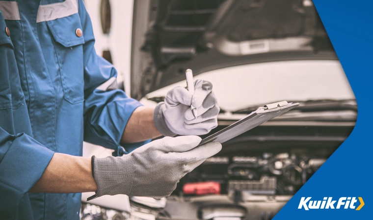 Auto technician performing diagnostic tests and writing down results on sheet attached to a clipboard.