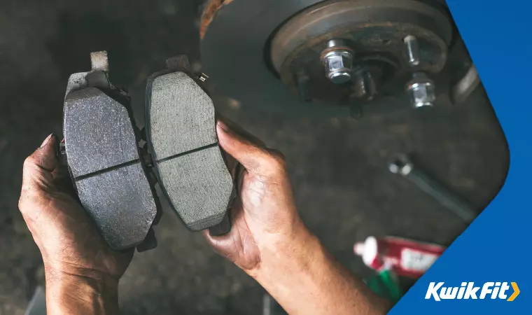 Someone holding new brake pads next to old, worn down ones.