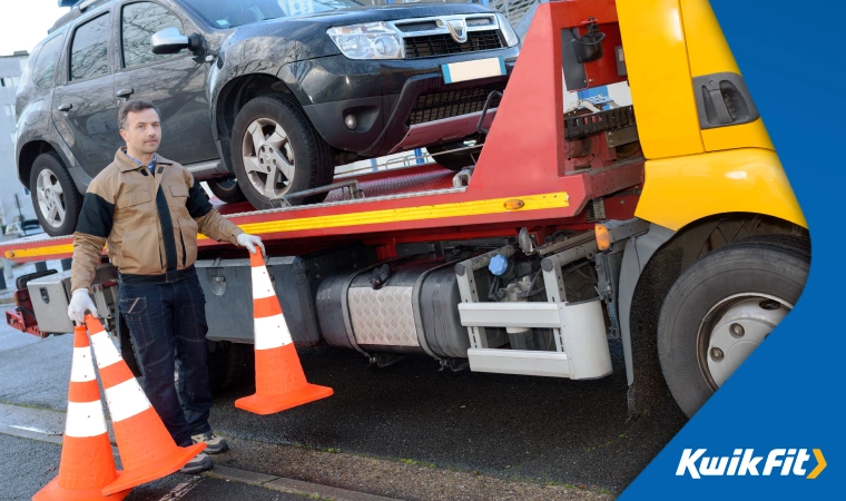  Breakdown assistance worker clearing up traffic cones after having lifted a broken down car onto the back of a tow truck.