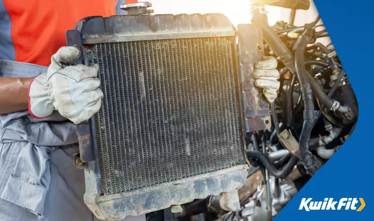 A technician holds a faulty car radiator after having removed it from a vehicle.