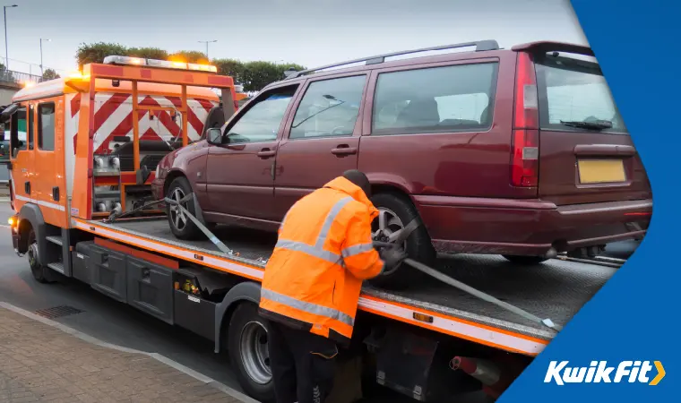 A car being hitched onto a flat-bed recovery lorry.