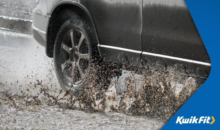 Muddy rain water splashing up on to a car as it drives through a big puddle.