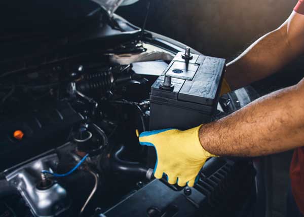 Technician wearing yellow gloves removing a car battery from a car.