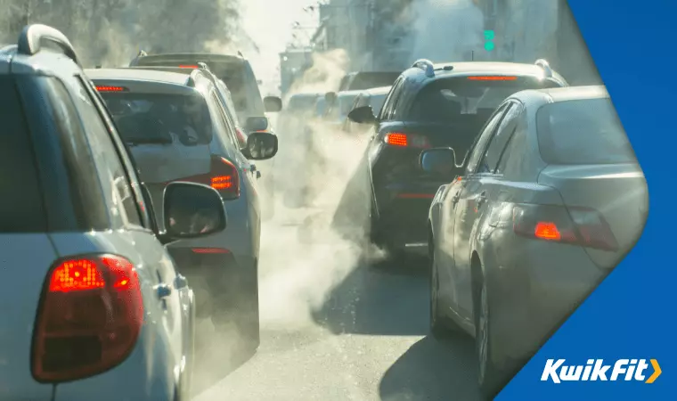 Cars are stuck in traffic and their exhausts release visible emissions, making the air foggy.