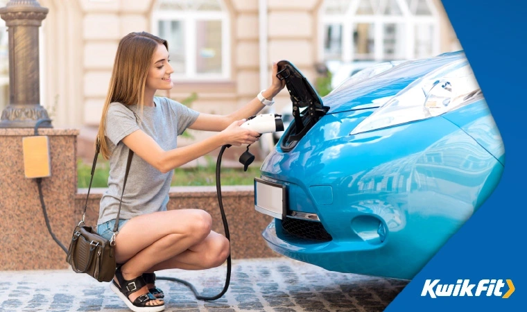 Young woman kneels to plug in a light blue electric or hybrid vehicle.