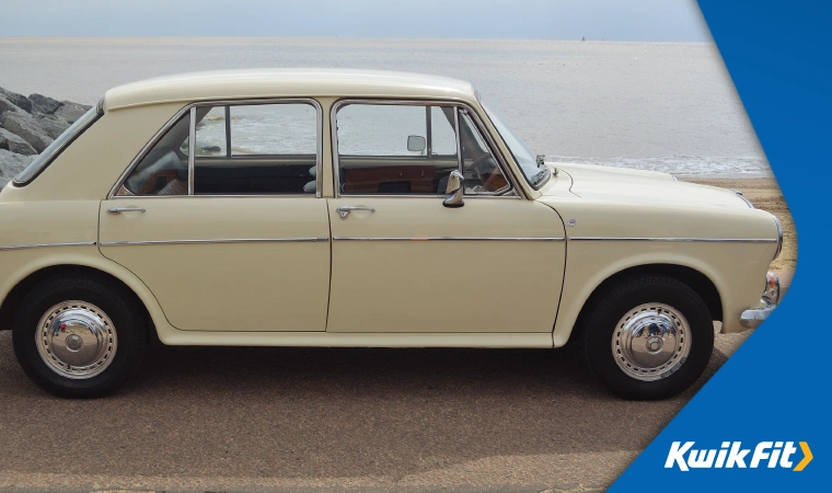 A classic Austin 1300 pictured on a typical British beach promenade, with sand and sea behind.