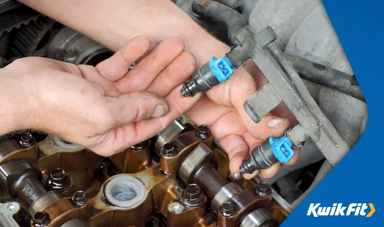 A technician's hands holding replacement fuel injectors for a petrol engine.