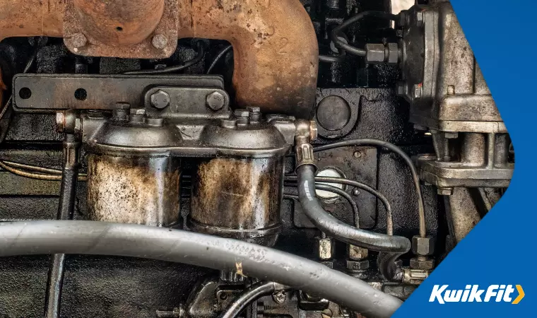 A car's engine bay, very grimy, showing slight leaks around the diesel filter.