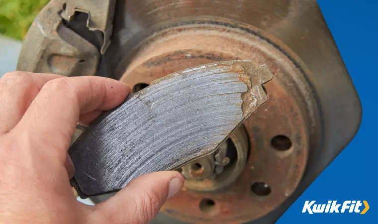 A technician inspects a heavily worn brake pad, likely in need of replacement.