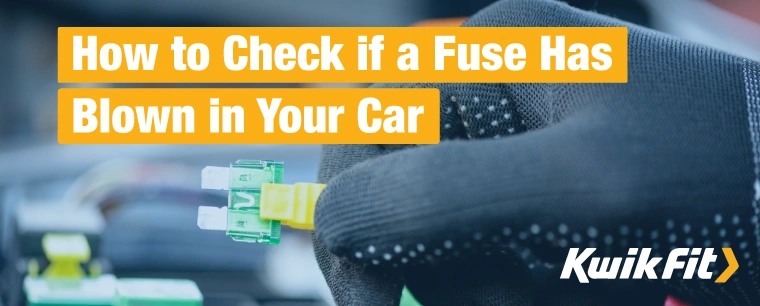 A gloved hand uses a fuse puller to remove a green fuse from a fuse box in a car.