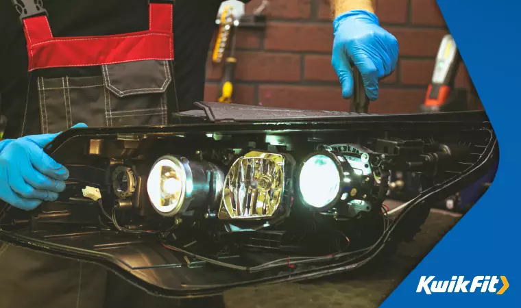 A mechanic inspects a removed headlight mount.