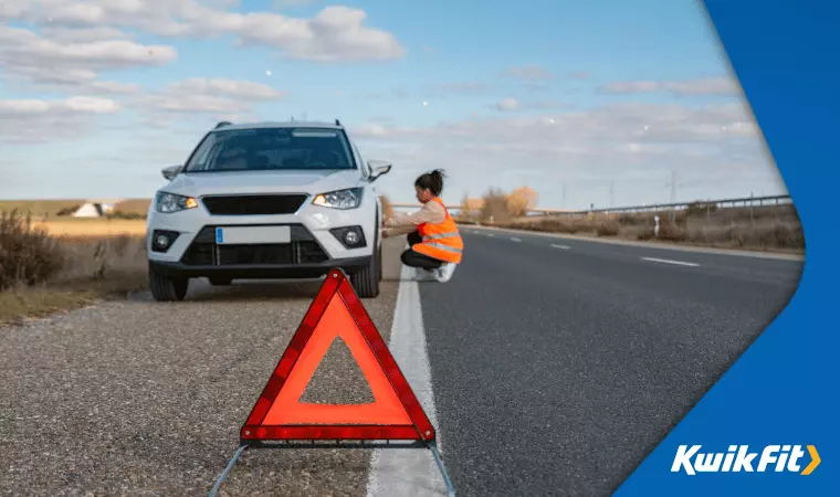 A person wearing a high-vis jacket has placed a warning triangle in front of their car.