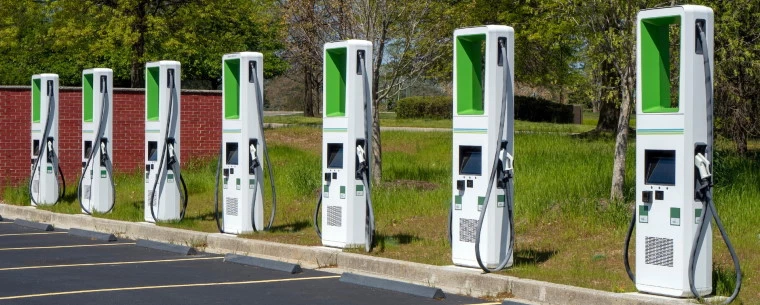 A line of green electric vehicle chargers stand in front of parking spaces waiting for use.