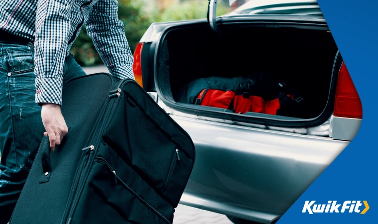 A person loads a large suitcase into the boot of their car.