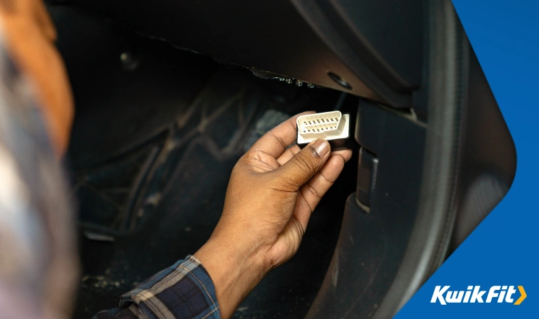 A driver inspects an OBDii port located in the footwell of a car.