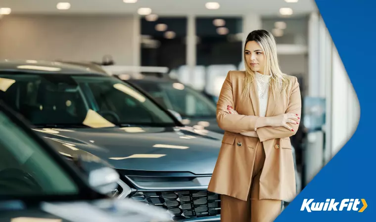 A person in a stylish tan suit looks around a car dealership showroom.