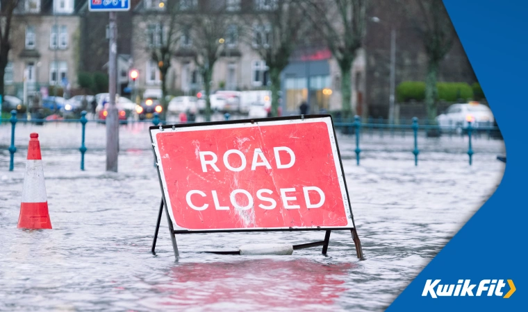 British Road Closed sign surrounded by flooding in a town or city.