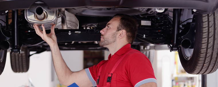 Technician with Clipboard Inspecting Car Exhaust 