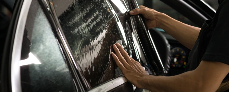 Worker applying tinted window film to vehicle