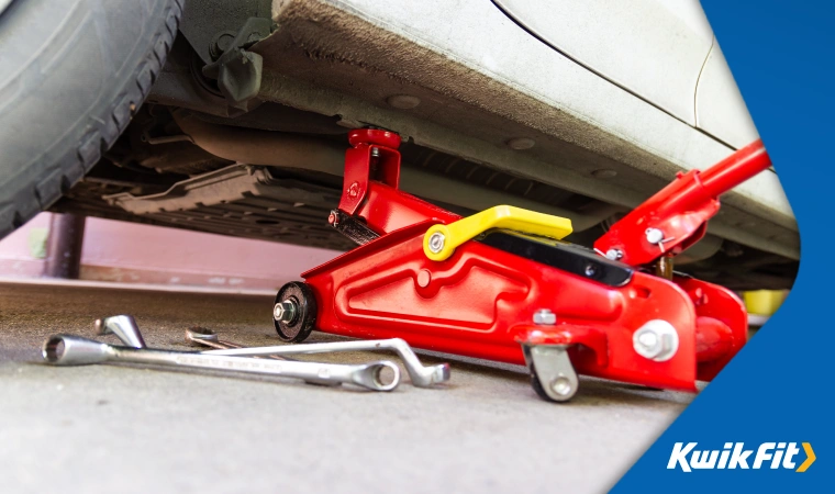 Glossy red hydraulic trolley jack used to raise a car using the correct jacking point.