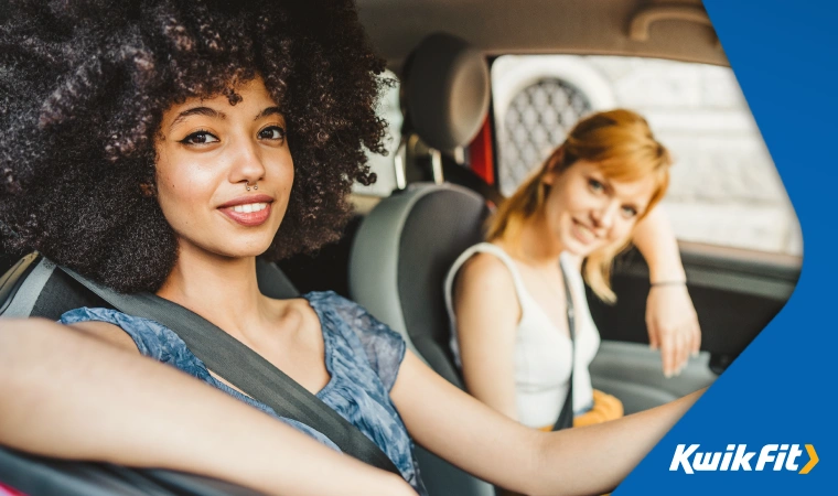 Two young people in a car smile at the camera, presumably happy with the freedom that driving gives them.