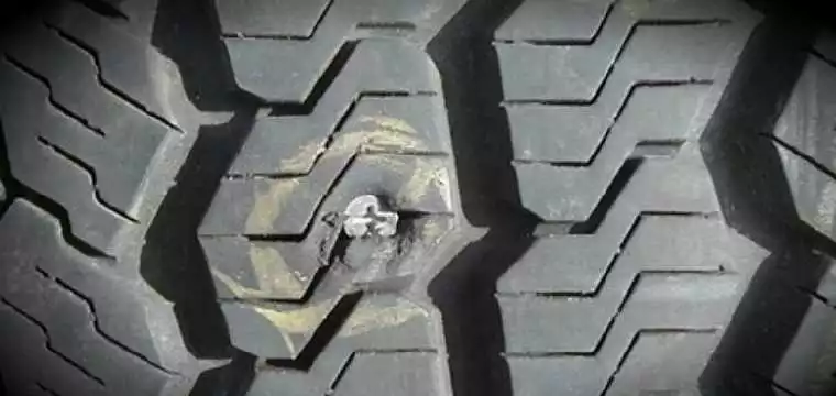 A tyre with a screw wedged in the rubber, causing a puncture.