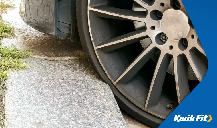 A car is parked with its tyre squashed against the kerb.