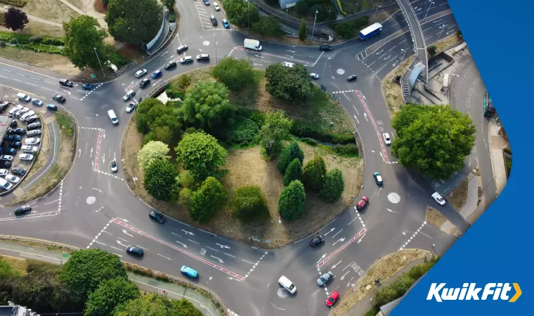A UK magic roundabout with a tree-studded central island built over a small watercourse.
