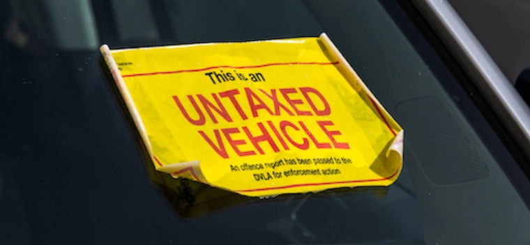 A yellow sticker is stuck to the windshield of a car. The sticker reads "This is an untaxed vehicle".