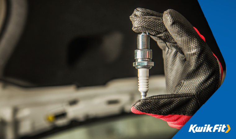 Technician wearing black and red gloves holding a spark plug.