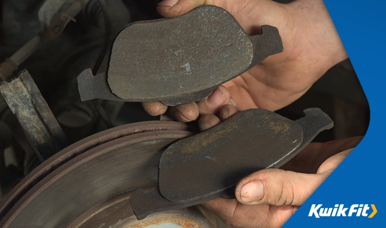 A technician inspects heavily worn brake pads, removed from what appears to be an aged brake disc.