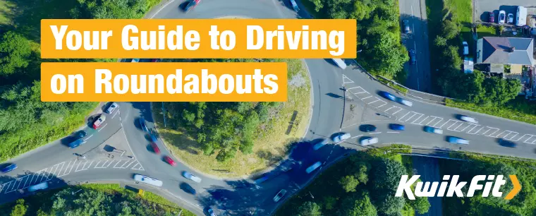 Aerial view of a one-lane roundabout surrounded by green, tree-lined verges.